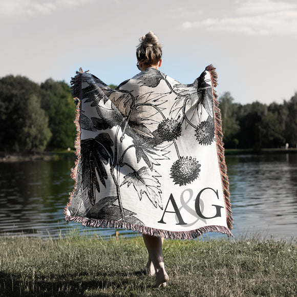 Woman draped in woven cotton throw blanket with floral leaves and monogram initials woven into the blanket.
