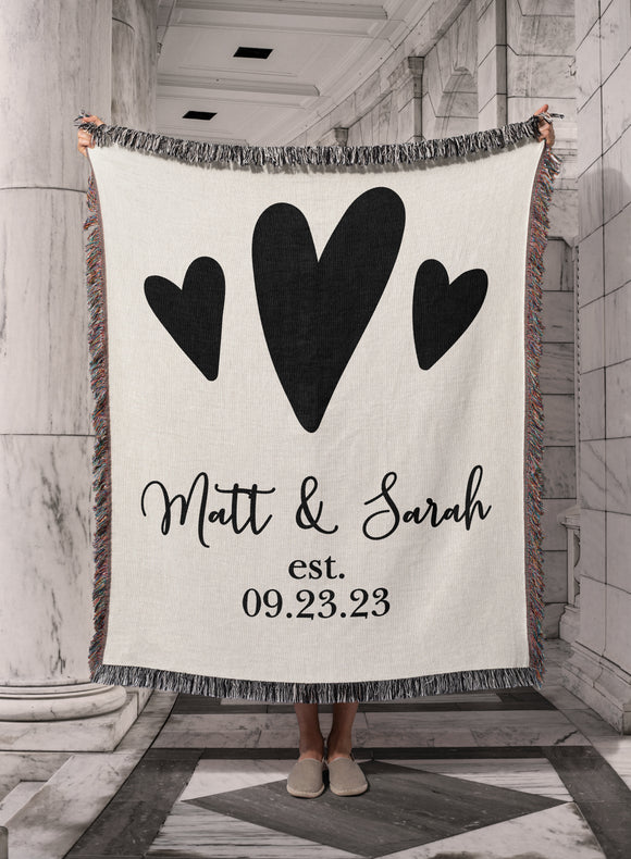 Personalized Woven Cotton Wedding Anniversary Throw Blanket, with soft white background and 3 hearts. Personalized with script style font first names separated with heart and established date. Made in the USA