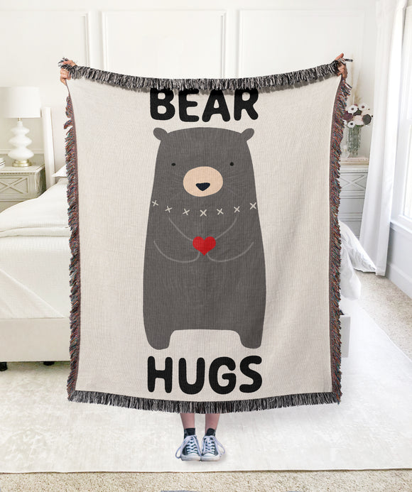 Bold Text phrase of Bear Hugs on top and bottom of blanket with cute bear holding heart in the center. Woven cotton blanket. Made in USA