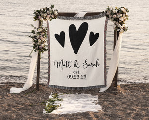 Woven throw blanket with one big heart and two small hearts. Personalized with couples names and wedding or anniversary date. Woven in black text and hearts with soft natural woven background. 